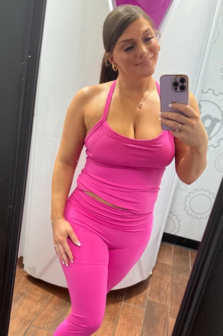 The woman behind DirtyCouple52 in a pink workout set, mirror selfie