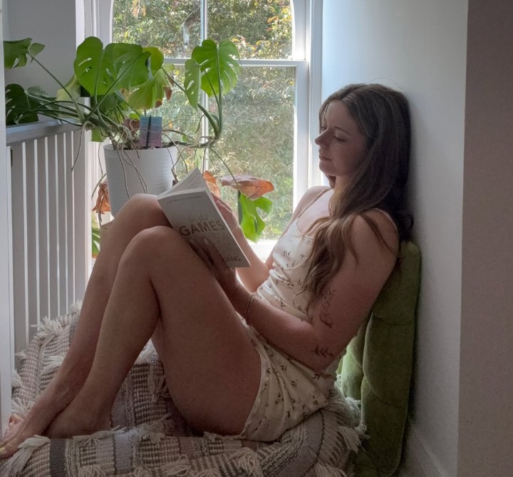 Nadia Foxx, a Canadian OnlyFans MILF creator relaxing with a book by a window
